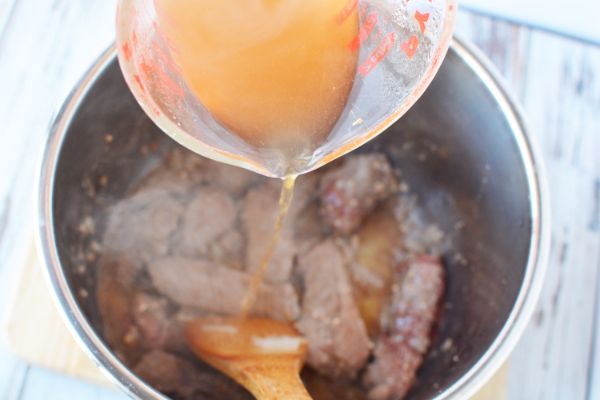 pouring sauce from a glass measuring pot into an instant pot filled with beef