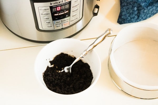 crushed oreos in a white bowl with a spoon in it next to a springform pan and an instant pot
