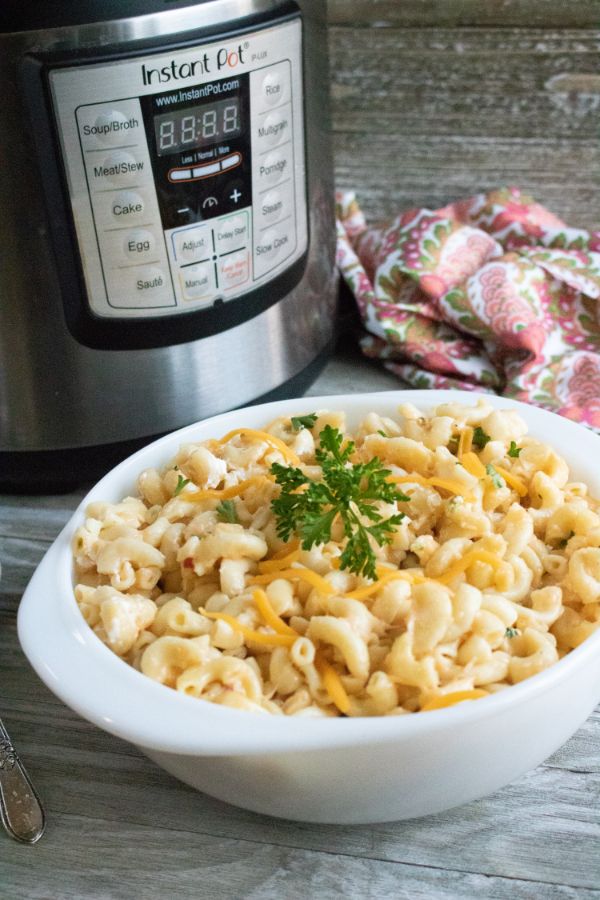 a white bowl of mac and cheese topped with parsley on a brown table next to an instant pot