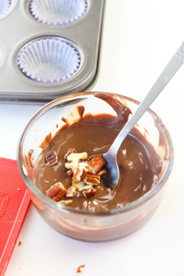 a glass bowl with a spoon in it, and chocolate, nuts, and pomegranate seeds on a white background with cupcake liners and a muffin tin in the background