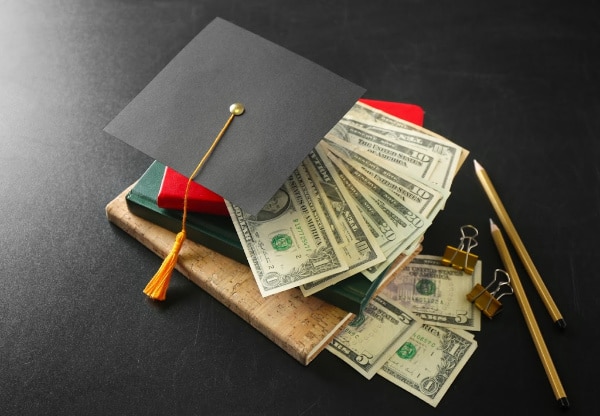 a graduation cap, money, books, pencils, binder clips on a black background