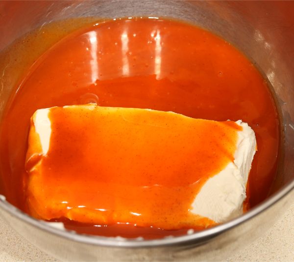 cream cheese in a metal mixing bowl covered with hot sauce