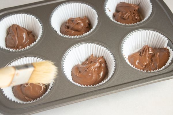 a pastry brush above a muffin tin filled with paper muffin liners filled with melted chocolate