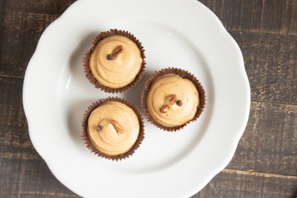 top view of chocolate cups filled with pumpkin mousse topped with nuts and a chocolate chip on a white plate on a brown table
