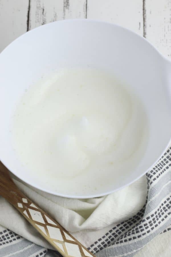 frothy egg whites in a white mixing bowl on a white wood table with a gray linen next to them