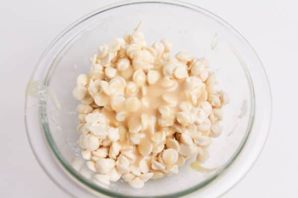 white chocolate chips covered with condensed milk in a glass bowl on a white background
