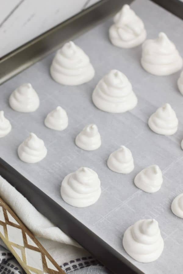 meringue batter piped onto a parchment paper on a baking sheet to look like ghosts