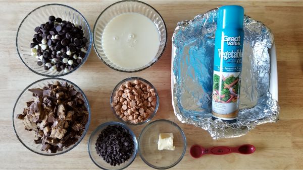 ingredients for Reese's Peanut Butter Fudge in the Instant Pot, like chocolate chips, reeses peanut butter cups, peanut butter chips, butter, vegetable oil spray in a pan wrapped in aluminum foil, and a measuring spoon