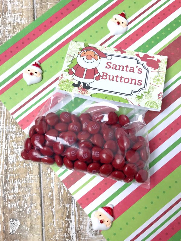 a plastic bag filled with red m&ms with a Santa's Buttons label on a red, green & white striped paper with mini Santa faces on it