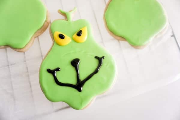 a cookie shaped like the Grinch with green frosting and yellow frosting with black gel on that to look like eyes and a mouth