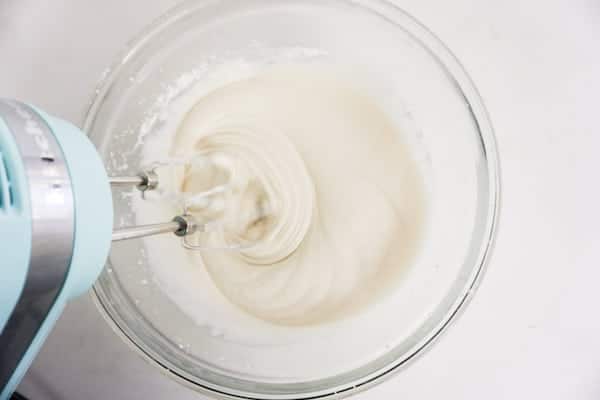 using a hand mixer to mix the icing ingredients in a glass mixing bowl on a white counter