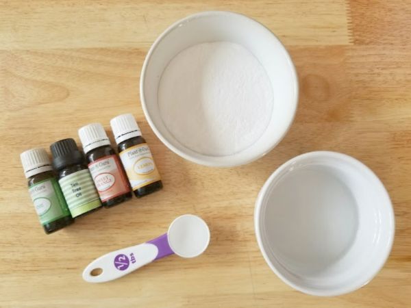 jars of essential oils, bowls of baking soda and dish soap, a measuring spoon, all on a table