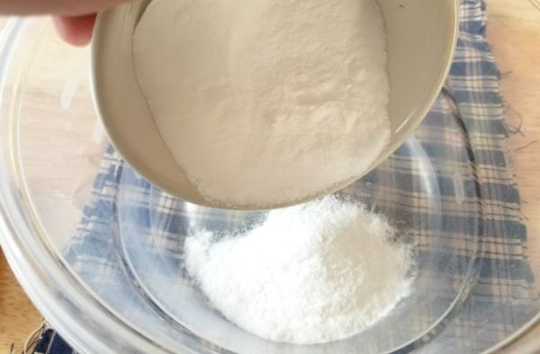 adding baking soda from a small bowl to a larger glass bowl