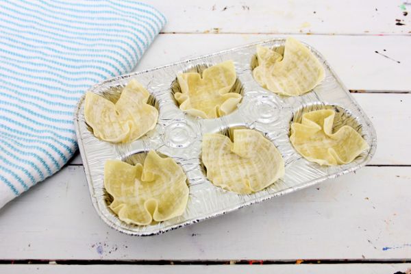 wonton wrappers in a muffin tin on a white table with a blue and white striped linen next to it