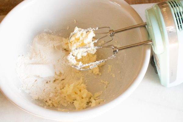 flour and dough in a white mixing bowl with a hand mixer over it
