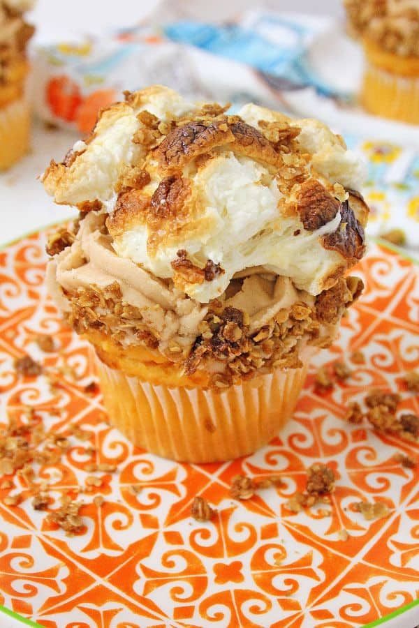 sweet potato cupcake topped with frosting, crumble topping and marshmallows on an orange and white plate