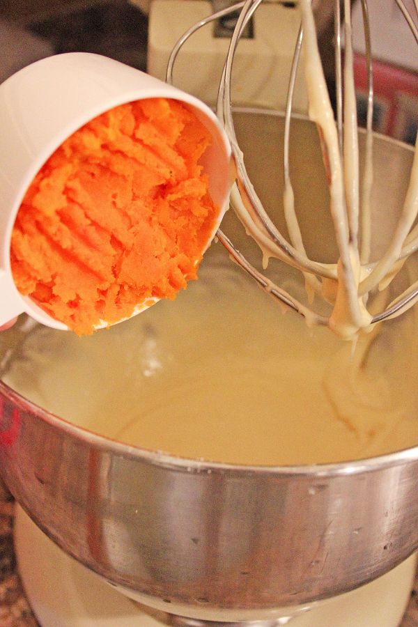 sweet potato from a white measuring cup being added to a miking bowl of cupcake batter