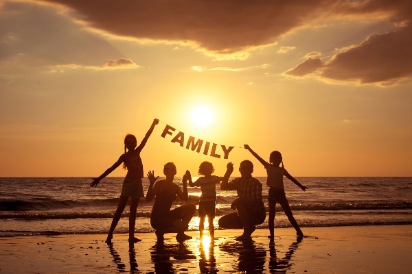 family standing on a beach taking a group portrait at sundown with a family sign