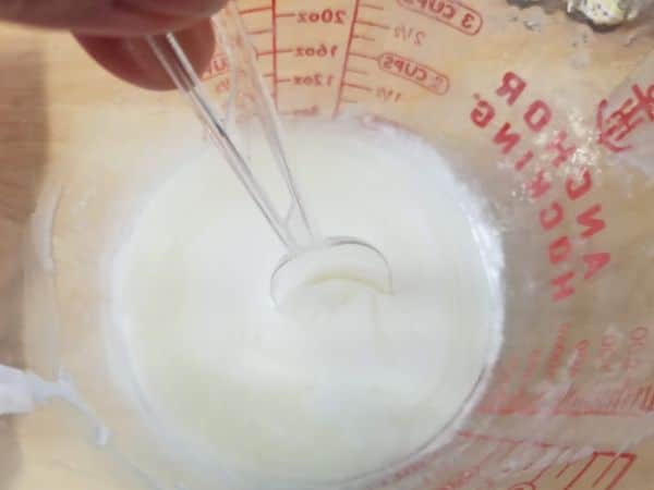 melted goat's milk soap base in a glass measuring cup being stirred with a spoon