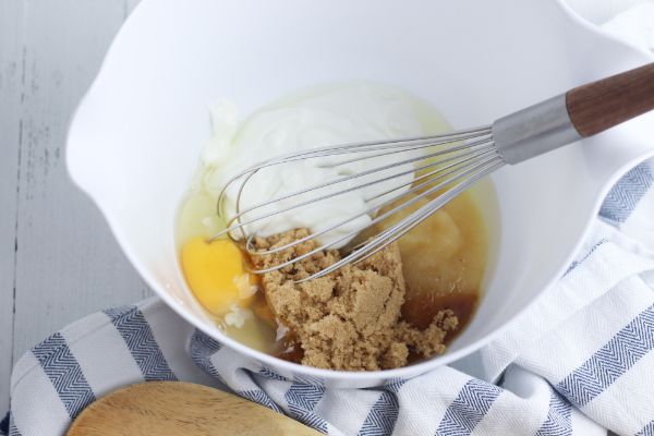 applesauce, brown sugar, egg, plain nonfat Greek yogurt, and vanilla extract in a white mixing bowl with a whisk in it