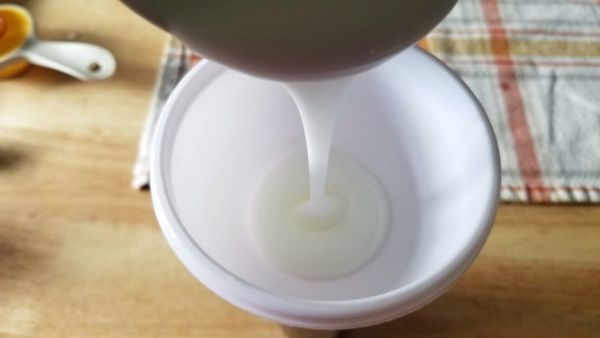 homemade lice spray being poured into a white funnel on a brown table