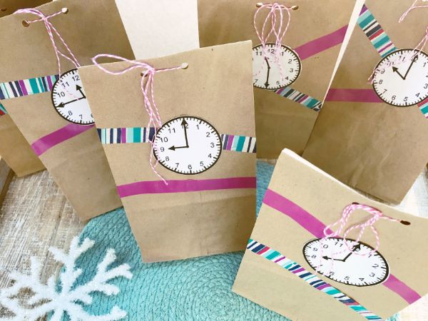 paper bags with paper clocks glued on them and ribbons with a snowflake in the background on a green linen