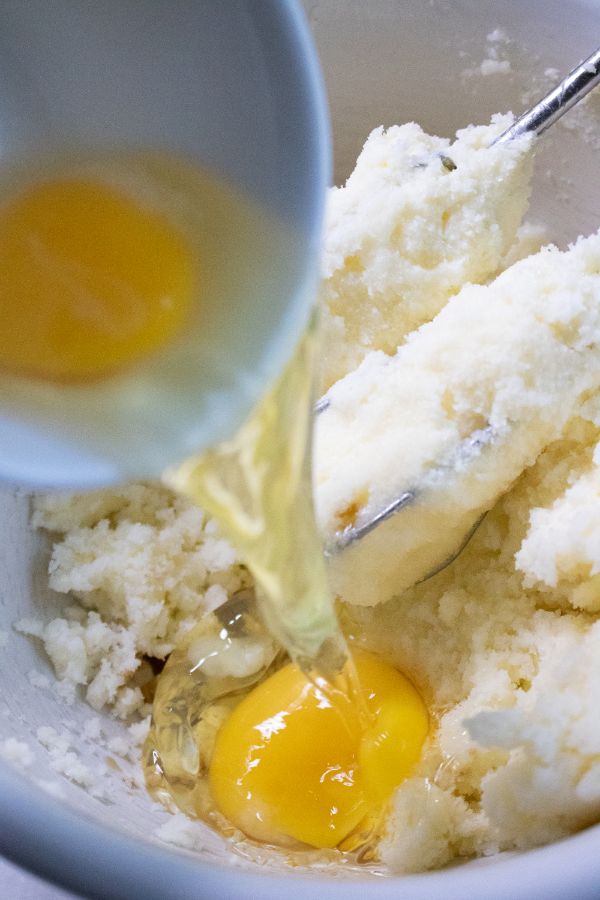 eggs pouring out of a small bowl into a mixing bowl full of batter