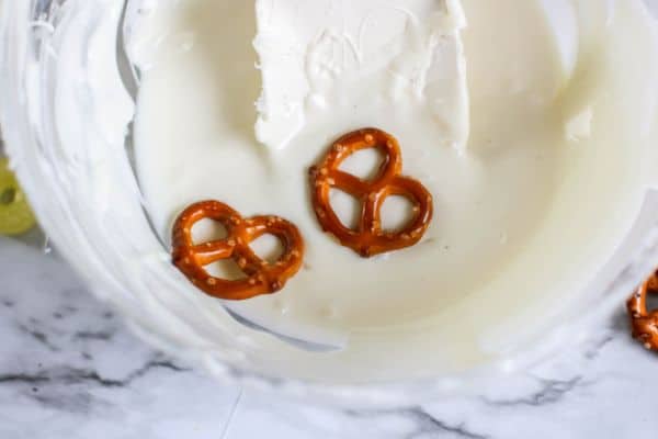 a glass bowl full of melted white chocolate with two pretzels on the top