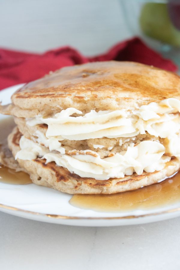 Apple Cheesecake Pancakes topped with syrup on a white plate