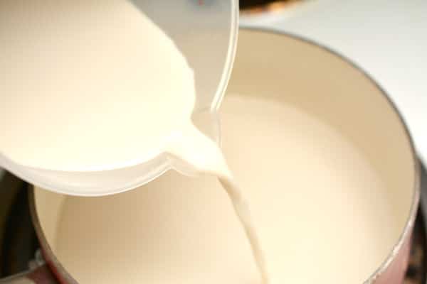 unsweetened vanilla almond milk being poured from a measuring cup into a pan