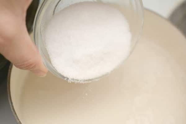 erythritol being poured from a glass bowl into a pot of almond milk