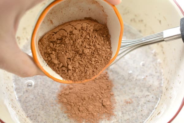 unsweetened cocoa powder being poured from a bowl into a bowl of chia seeds and almond milk