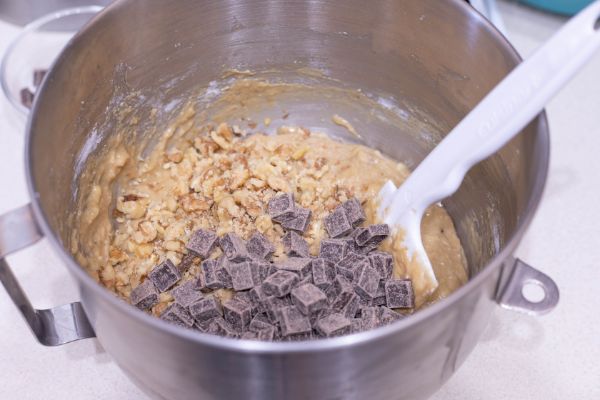walnuts and chocolate chunks added to the batter for chunky monkey muffins in a metal mixing bowl with a white spatula in it