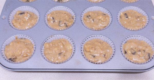 chunky monkey muffin batter in white muffin liners in a muffin pan