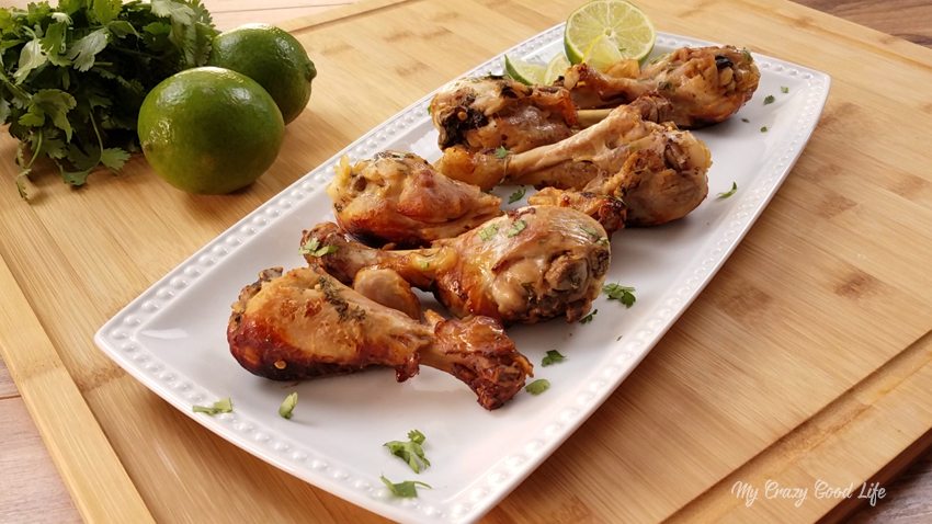 cilantro lime chicken drumsticks on a white platter on a wood table next to limes and a bunch of cilantro