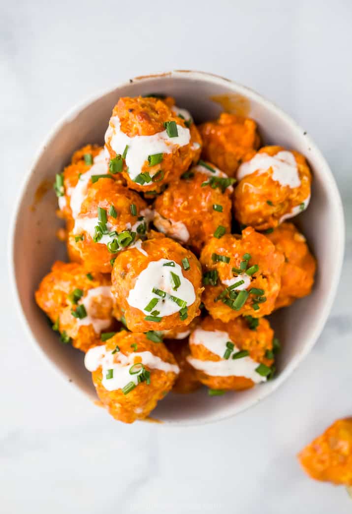 buffalo chicken meatballs topped with sour cream and chives in a white bowl on a white counter