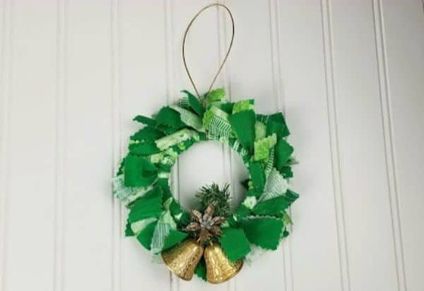a green fabric mason jar lid ornament with gold bells at the bottom of it on a white background
