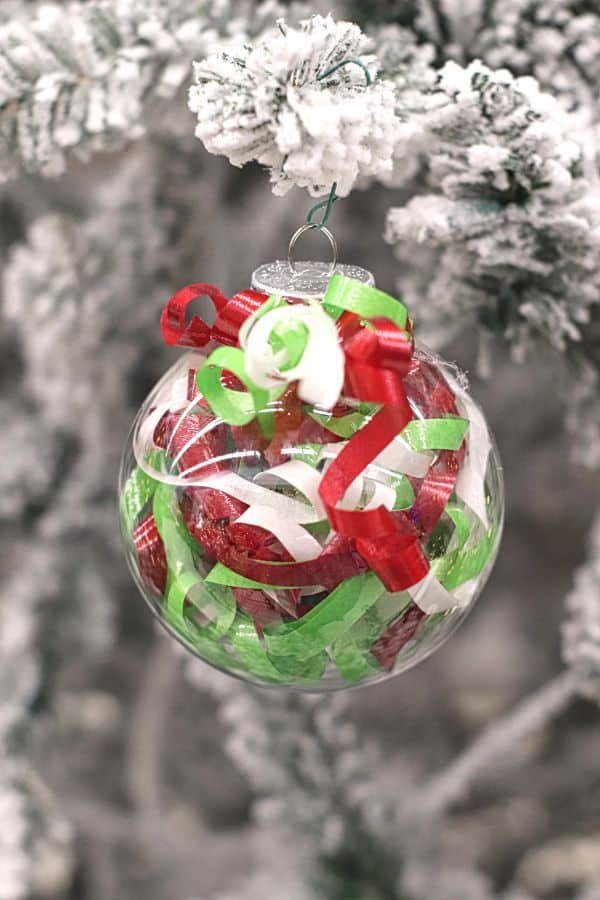 a clear ornament filled with curled ribbon hanging from a flocked Christmas tree