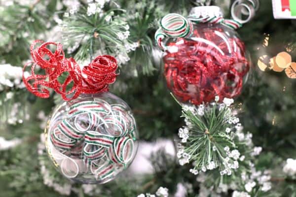 two clear ornaments filled with curled ribbon with a red and green ribbon curl on the top hanging from a Christmas tree