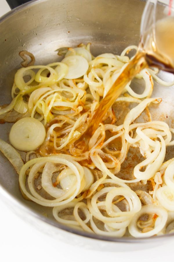 broth and balsamic vinegar being added to a skillet with sliced onions cooking in it