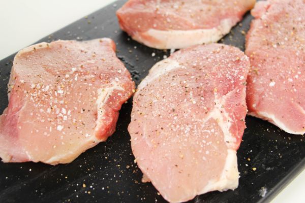 raw pork chops seasoned with salt, pepper, and herbs de Provence on a black board