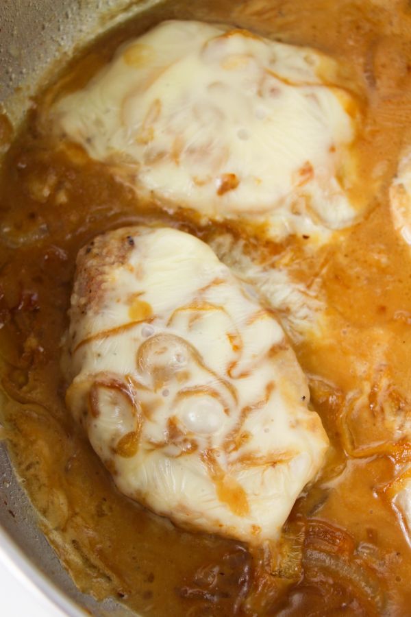 pork chops cooking in a skillet with gravy, topped with cheese and onions