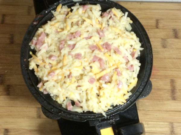ham and cheese hash brown waffles in a waffle maker on a brown table