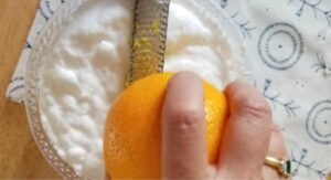 zesting orange over bowl of homemade kitchen cleaner