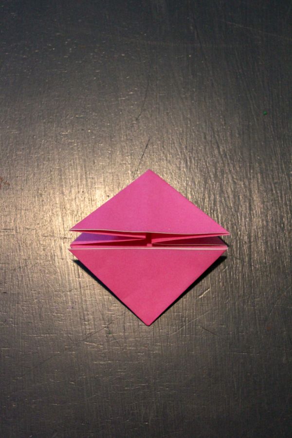 pink origami paper folded into two triangles on a dark brown background