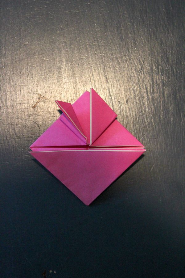 pink origami paper folded into triangles on a dark brown background