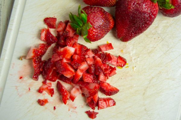whole strawberries and chopped strawberries on a white cutting board