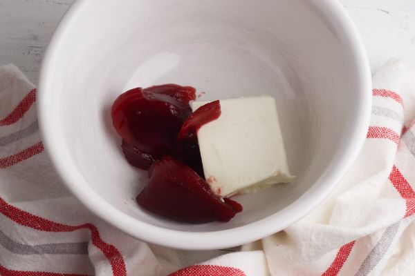 cream cheese and cranberry sauce in a white bowl next to a red and white cloth
