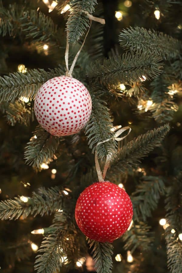 two ornaments wrapped with red and white washi tape hung with  gold ribbon from a  Christmas tree