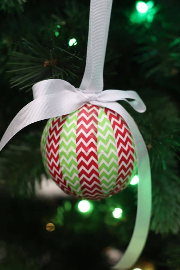 on ornament wrapped with red and green washi tape hung with a white ribbon from a Christmas tree